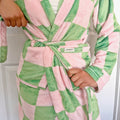 Person wearing a pink and green checkered robe with a brand label.